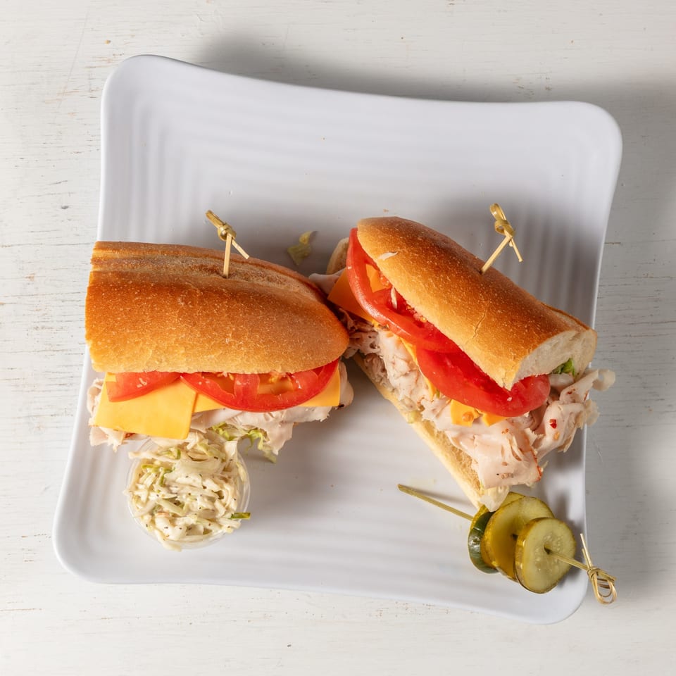 Two deli sandwiches with turkey, cheese, tomato, and lettuce, served with coleslaw and pickles.