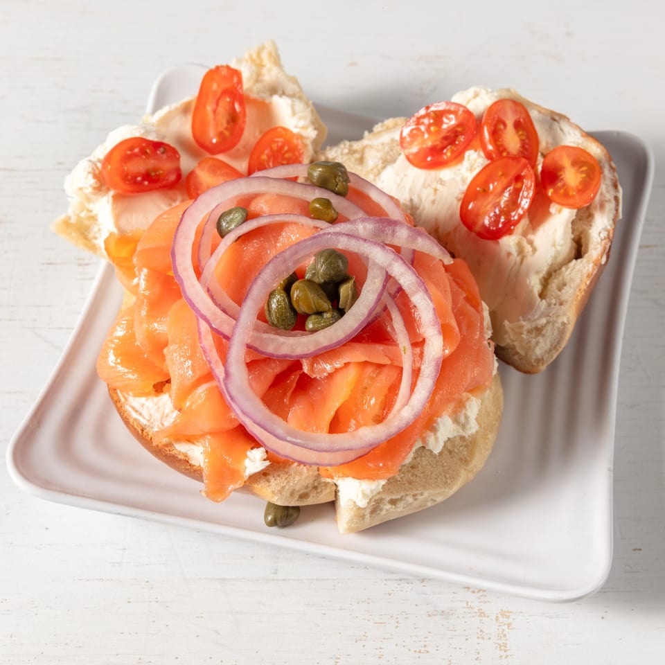 Two bagels with cream cheese, one topped with smoked salmon, red onion, capers, and the other with cherry tomatoes.