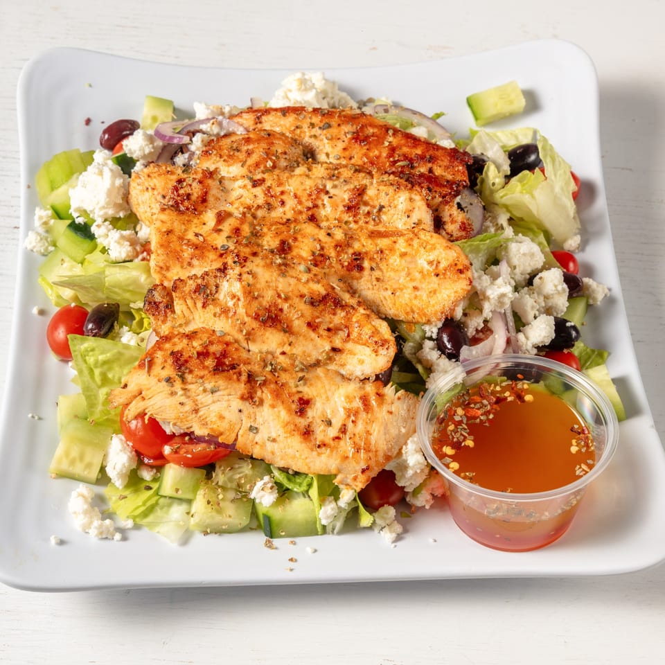 Grilled chicken breast over a fresh salad with feta, olives, tomatoes, and cucumbers, with dressing.