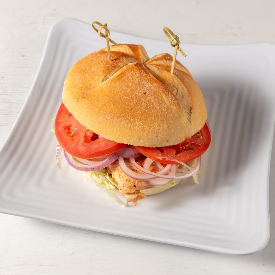Pierce Street Bagel Cafe Deli & Grill's chicken sandwich with lettuce, red onion, and tomato on a white plate.